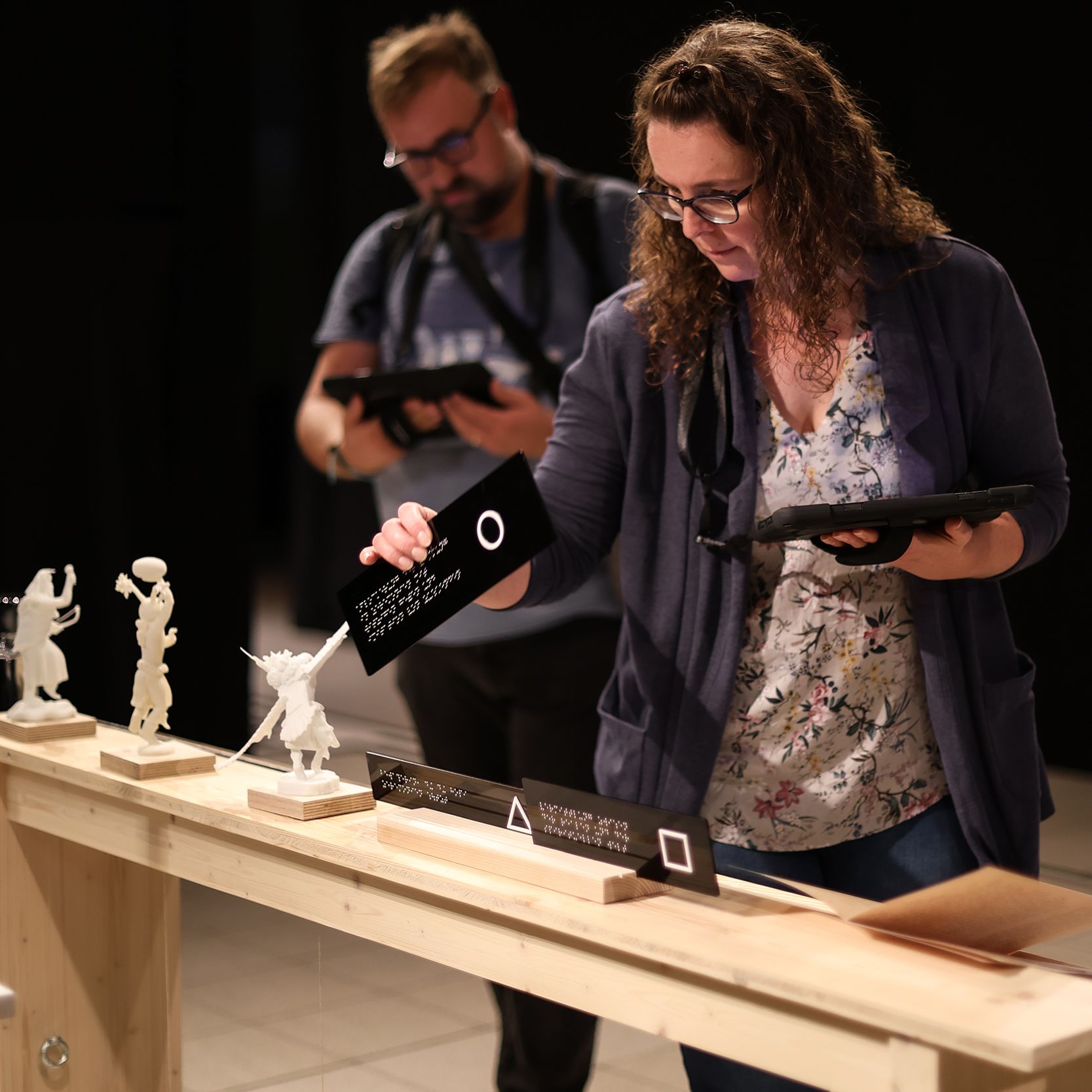 ein Mann und eine Frau in der Ausstellung am Kachina-Tisch, beide mit Tablet in der Hand, Frau entdeckt Zuordnungsspiel