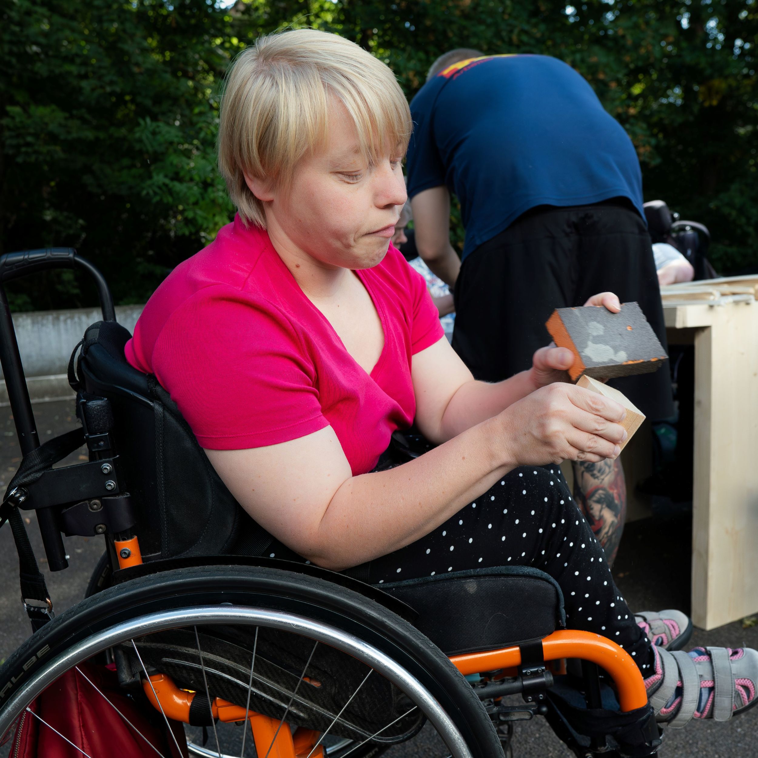 junge Frau im Rollstuhl schleift Holzklotz mit Schleifpapier