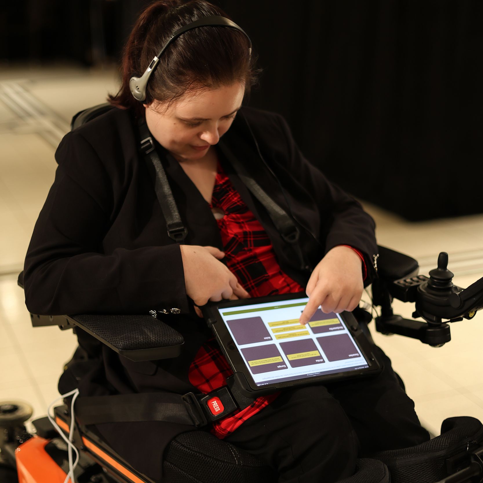 junge Frau im Elektro-Rollstuhl bedient Tablet mit Oberfläche des digitalen Ausstellungsguides